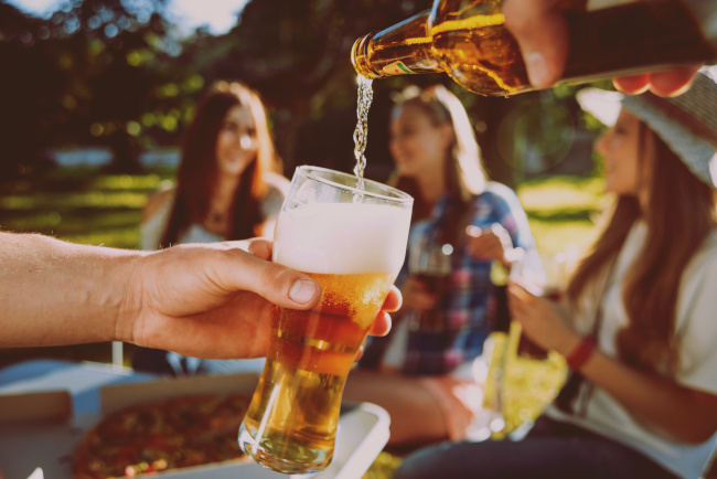 Gruppe vom Menschen sitzt im Park. Bier wird von einer Flasche in ein Glas geschüttet