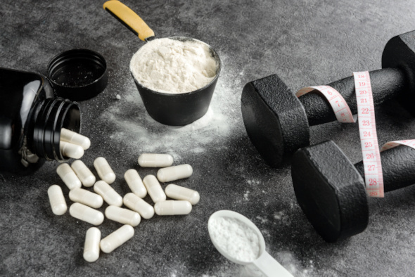 Protein-Scoop, Kreatin-Kapseln und Hanteln mit Maßband.