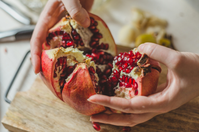 Person schält Granatapfel mit ihren Händen